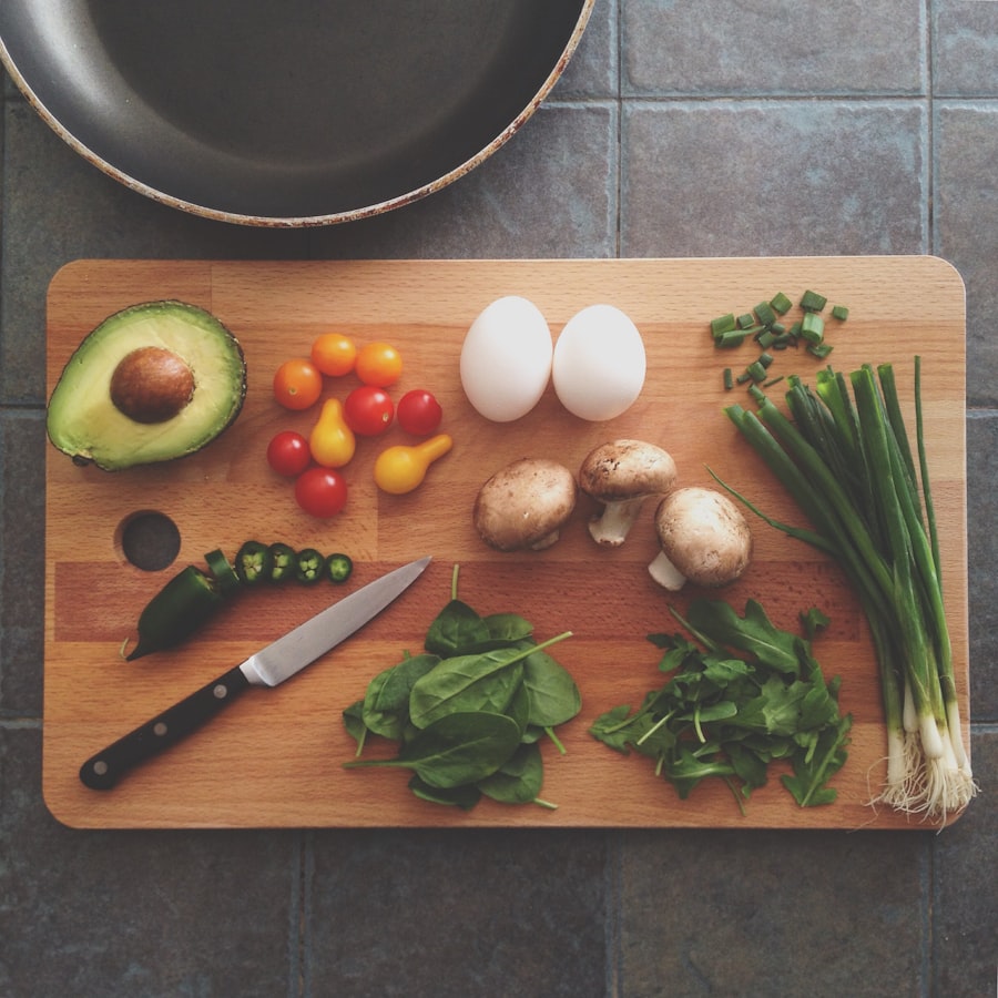 A cutting board of fresh ingredients: avocado, eggs, mushrooms, and greens laid out beside the skillet
